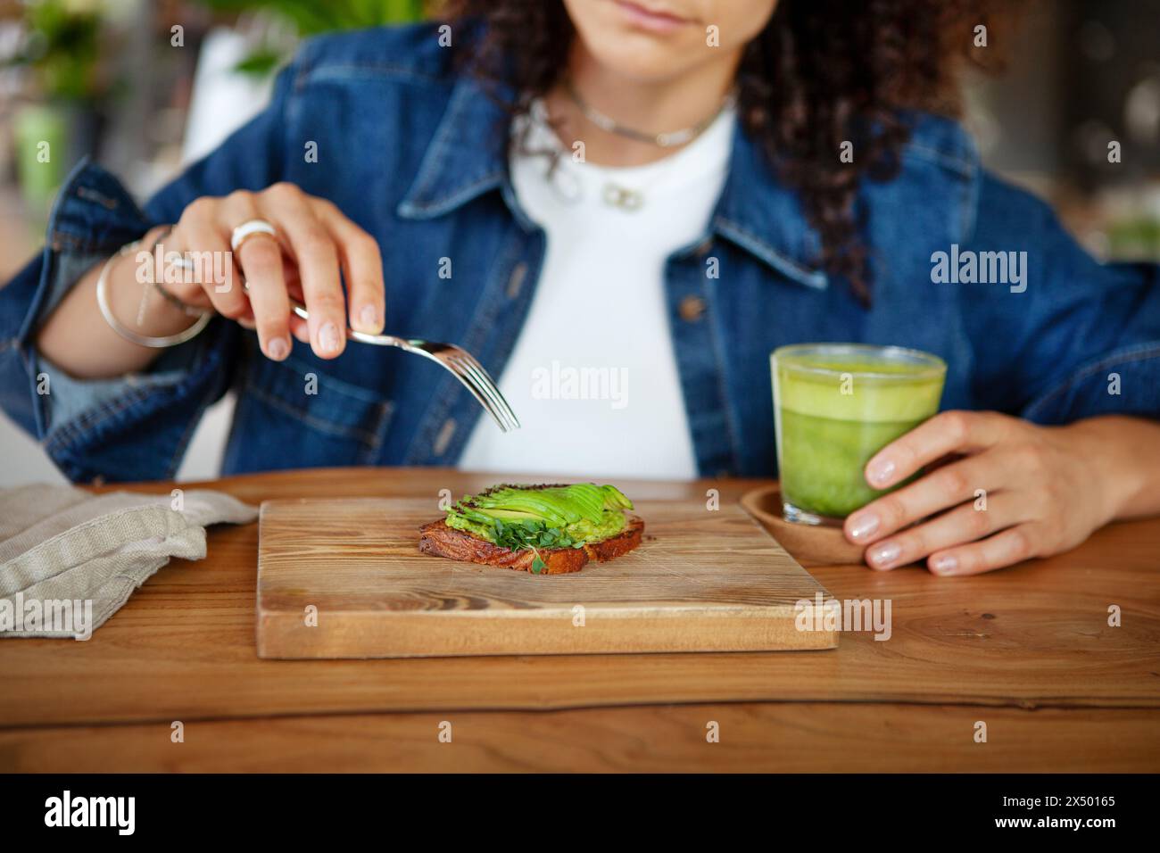 Frau genießt Avocado Toast und grünen Smoothie in einem Restaurant und bietet vegane gesunde Speisen. Stockfoto