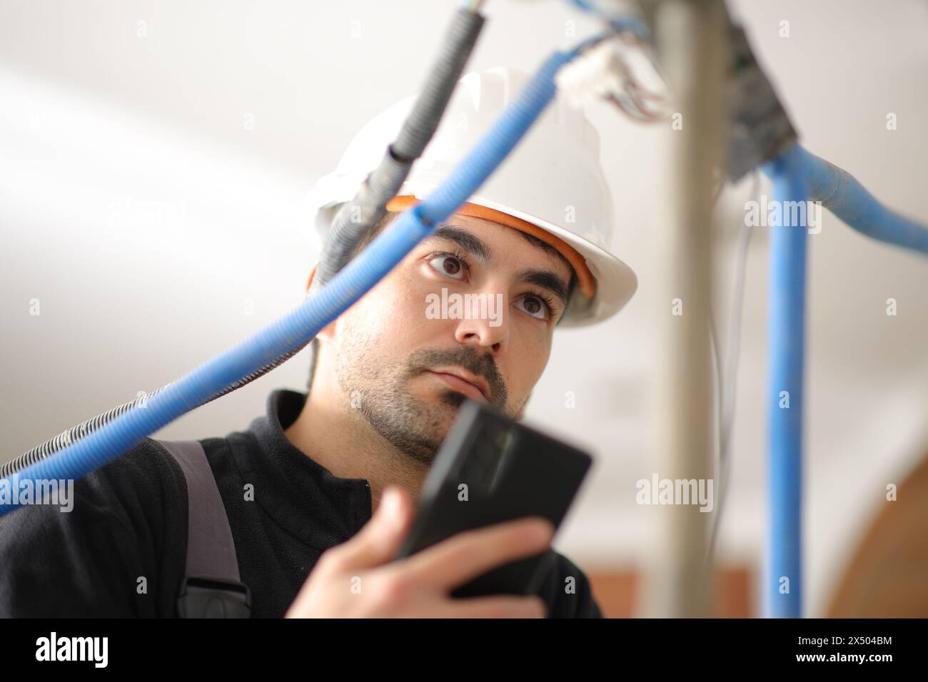 Elektriker überprüft die Installation mit einem Telefon in einem Haus im Bau Stockfoto