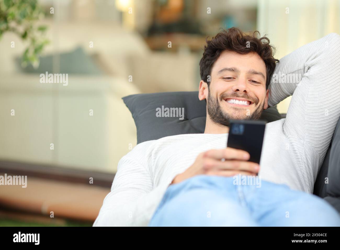 Glücklicher Mann, der auf einer Couch auf einer Terrasse liegt, mit dem Telefon Stockfoto
