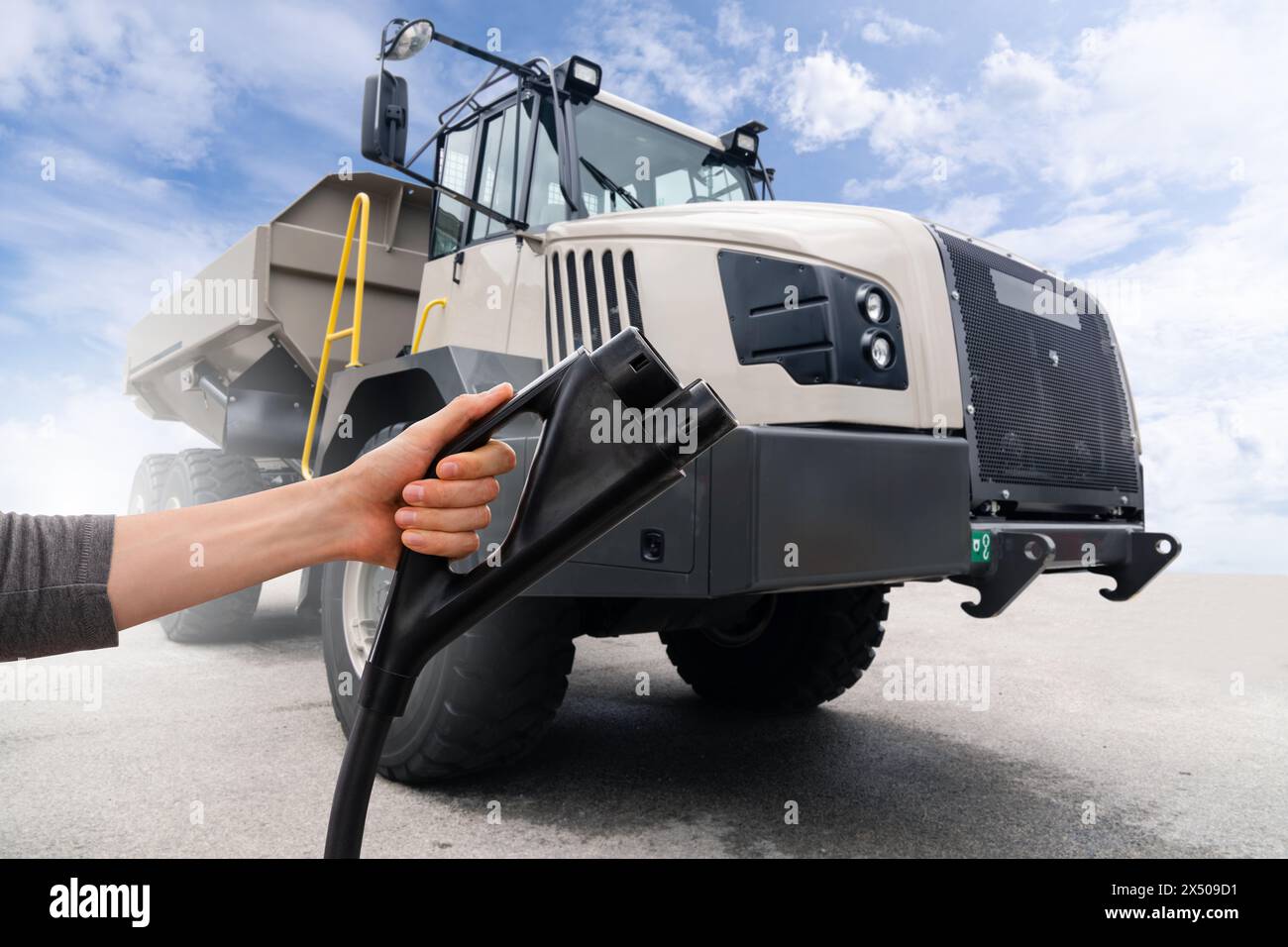 Hand mit Ladestecker auf einem Hintergrund eines elektrischen Bergbauwagens. Konzept Stockfoto