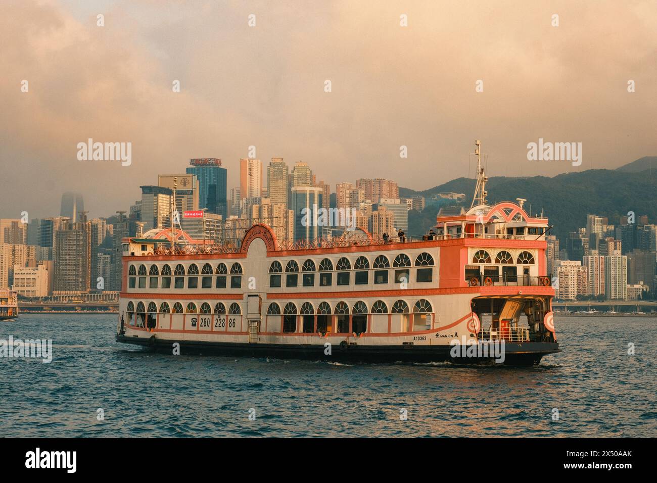 Bei genauerem Hinsehen offenbart sich die zeitlose Eleganz einer orangen Fähre der alten Schule, die durch den belebten Hafen von Hongkong fährt und Vintage-Charme mit verbindet Stockfoto