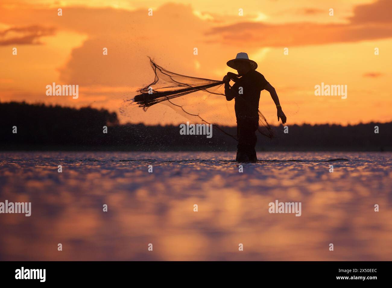Silhouette eines Fischers, der in einem Fluss steht und bei Sonnenuntergang ein Fischernetz wirft, Thailand Stockfoto