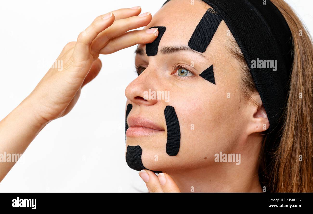 Gesichtsfalten-Reduktion und Hautstraffung. Frau Schönheitsmodell, das schwarze kinesio-Gesichtsbänder auf ihr Gesicht aufträgt, Nahaufnahme-Fotografie, Stockfoto