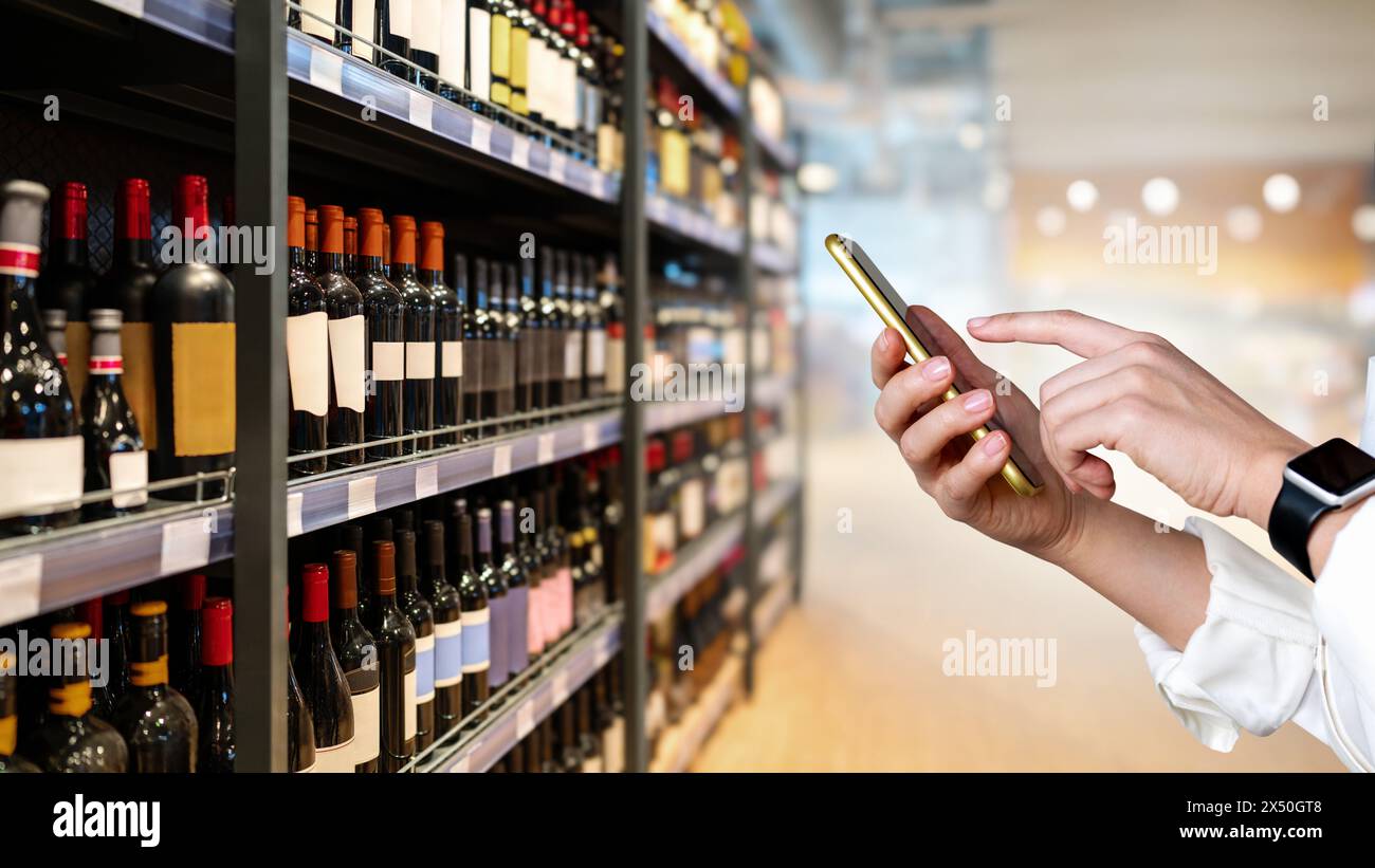 Wein online verkaufen. Internet-Bestellung von Wein und Alkoholprodukten. Geschäftsmann mit Smartphone im Spirituosengeschäft. E-Commerce und Einzelhandel. Stockfoto