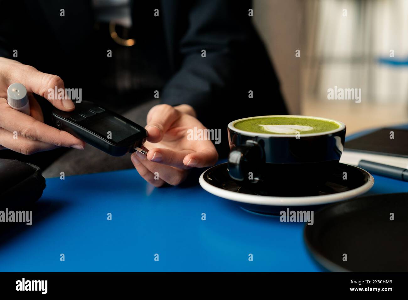 Nahaufnahme einer Frau, die den Blutzuckerspiegel in einem Café überprüft, bevor sie einen Matcha-Tee trinkt Stockfoto