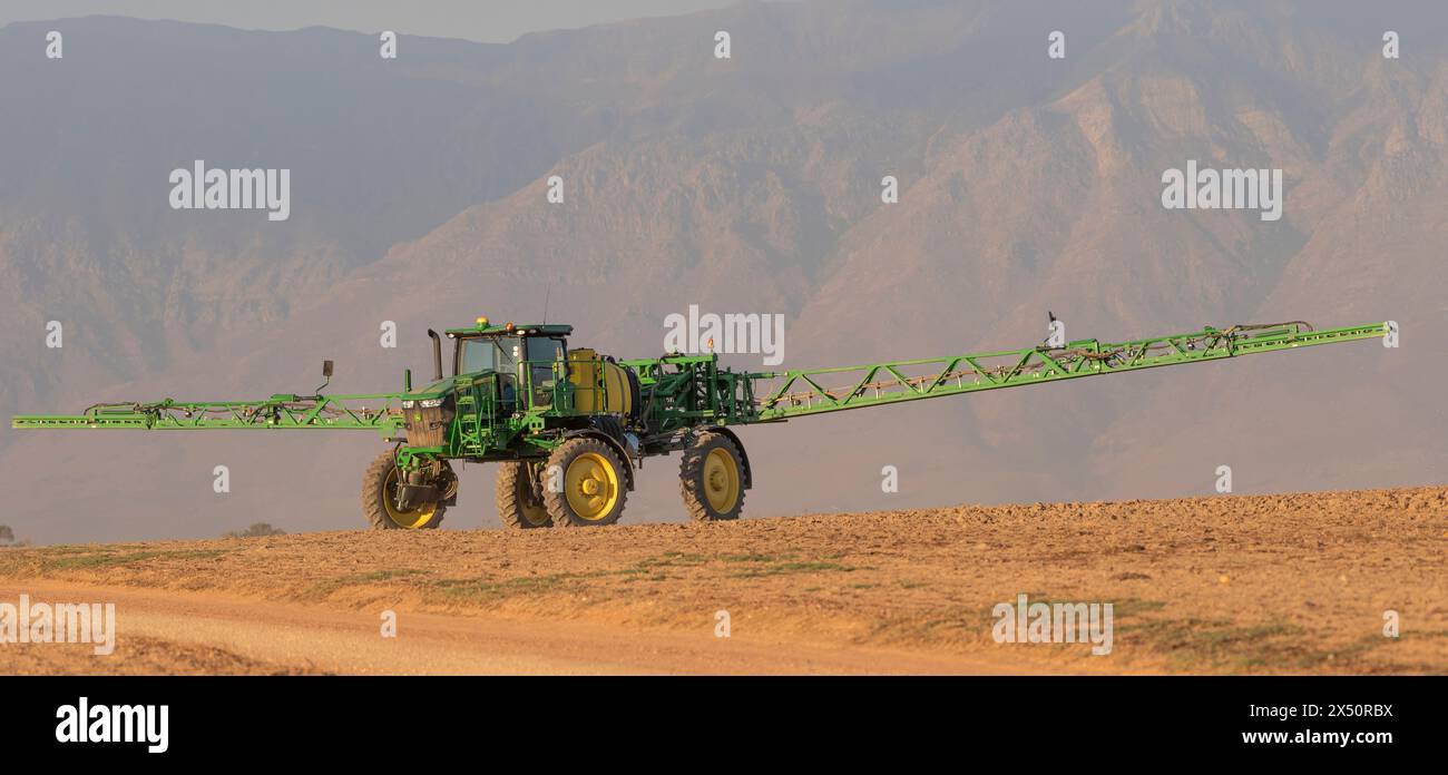 Westkap, Südafrika. April 2024. Traktor mit Auslegerarmen verlängertes Spritzen von Wasser, bevor eine Bohrmaschine Rapssamen auf fa pflanzt Stockfoto
