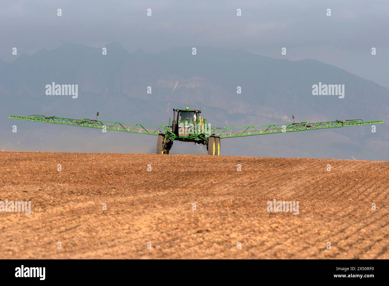 Westkap, Südafrika. April 2024. Traktor mit Auslegerarmen verlängertes Spritzen von Wasser, bevor eine Bohrmaschine Rapssamen auf fa pflanzt Stockfoto