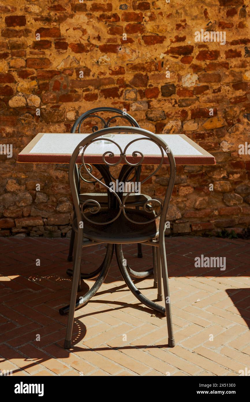 Ein Tisch mit zwei Stühlen in der Sonne auf der Hauptstraße der Altstadt von Certaldo - Certaldo Alto - in der Nähe von Florenz in der Toskana, Italien. Mit Ziegelwänden. Stockfoto