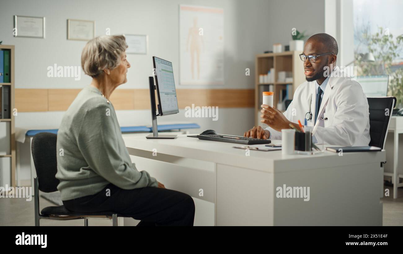 Afroamerikanischer Familienarzt verschreibt Medikamente für ältere weibliche Patienten und spricht mit ihr während der Konsultation in einer Gesundheitsklinik. Arzt sitzt hinter einem Schreibtisch im Krankenhausbüro. Stockfoto