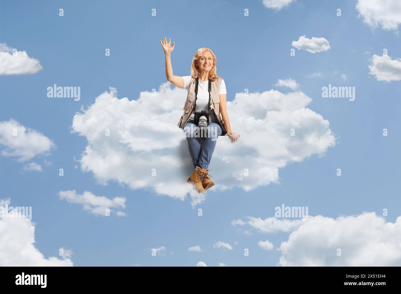 Weibliche Fotojournalistin sitzt auf einer Wolke und winkt Stockfoto