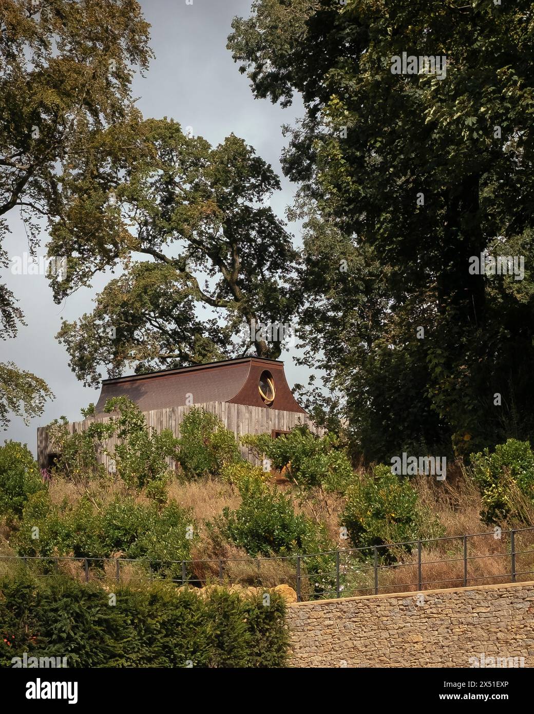 Der Apiary Pavillon, umgeben von Bäumen und Landschaftsgestaltung mit Badsteinmauer im Vordergrund. Das Beezantium am Newt, Bruton, Vereinigtes Königreich. Archit Stockfoto