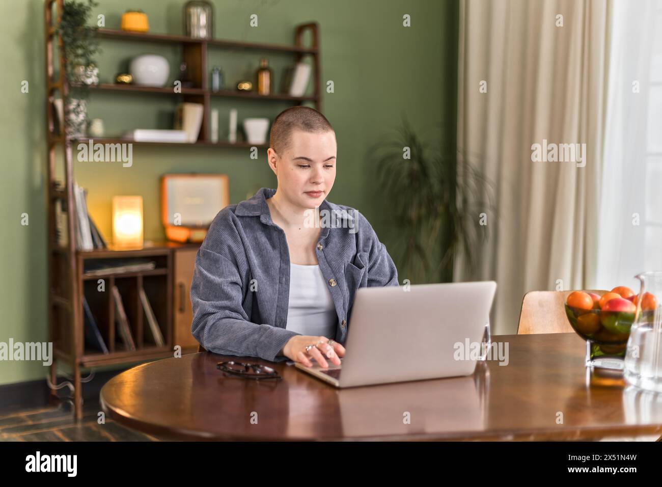 Junge kreative kahlköpfige Frau sitzt am Tisch und arbeitet ferngesteuert am Laptop Stockfoto