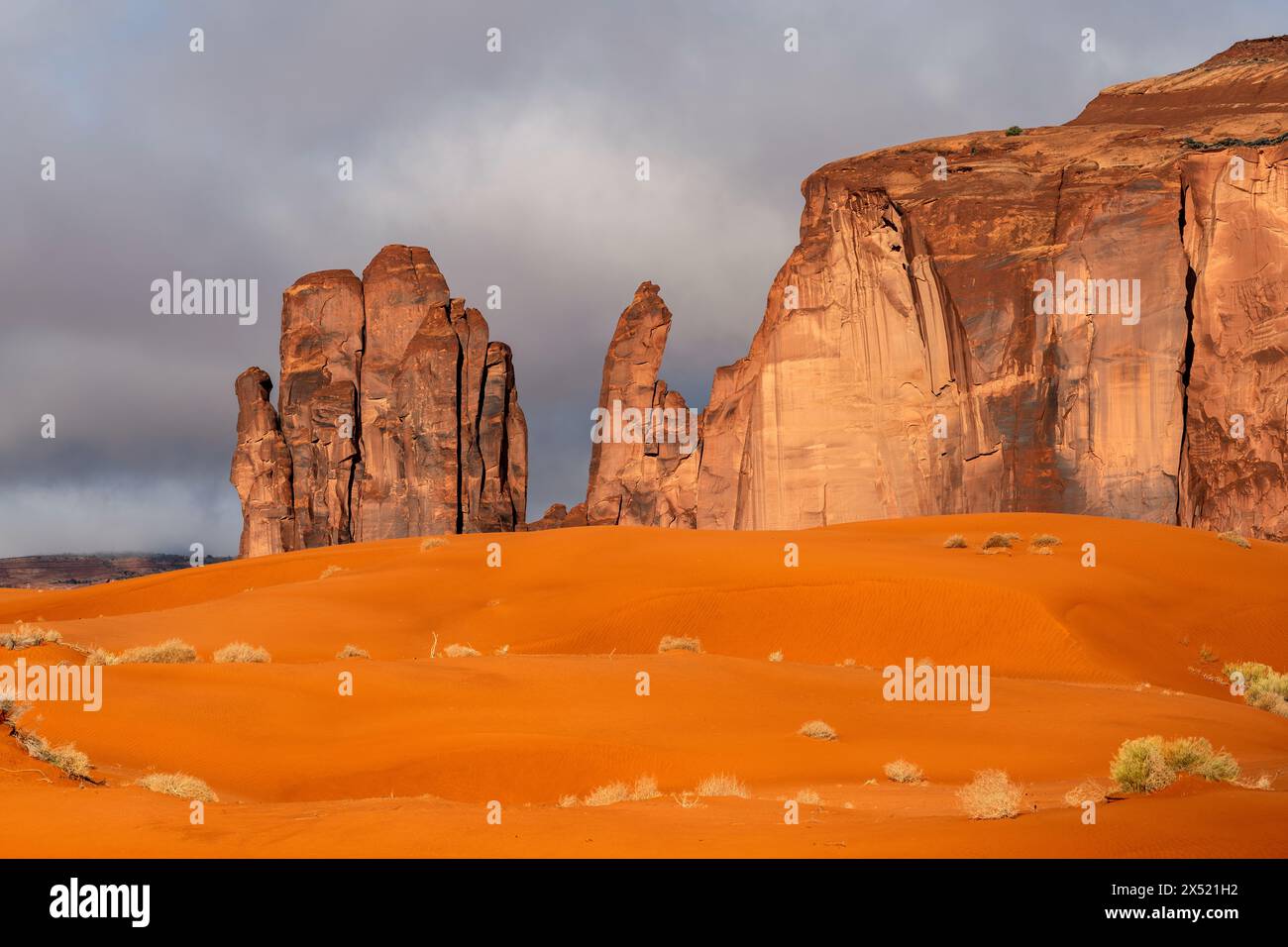 Die Wüstenlandschaft im Monument Valley Arizona zeigt einen Sonnenaufgang, der den Sand und die Berghänge in einem Orange färbt. Stockfoto