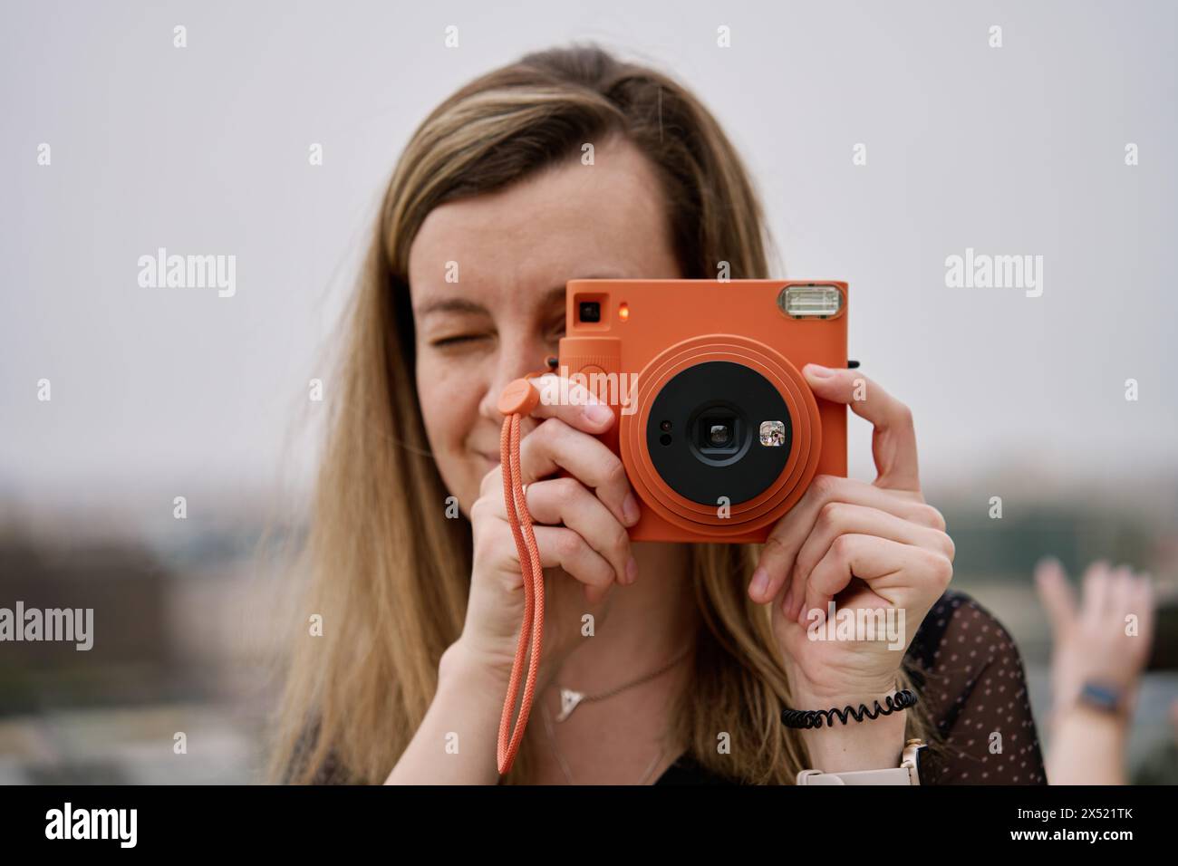 Frau, die Fotos mit orangefarbener Sofortkamera macht. Touristen halten Erinnerungen während der Reise mit einer alten Kamera fest Stockfoto