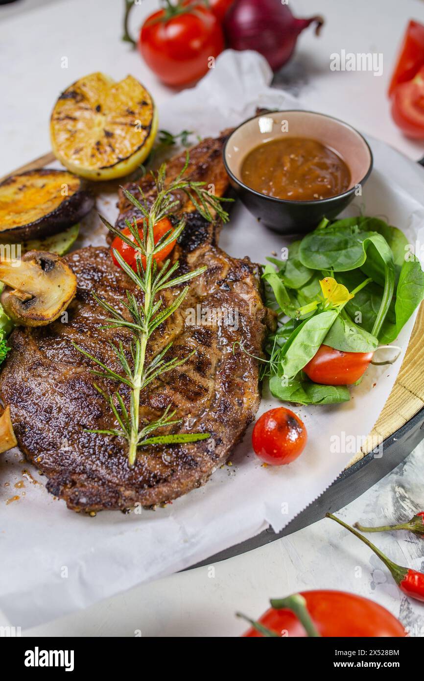 Ein saftiges und zartes gegrilltes Steak wird mit einer Vielzahl von geröstetem Gemüse serviert und mit einem Zweig Rosmarin garniert. Stockfoto