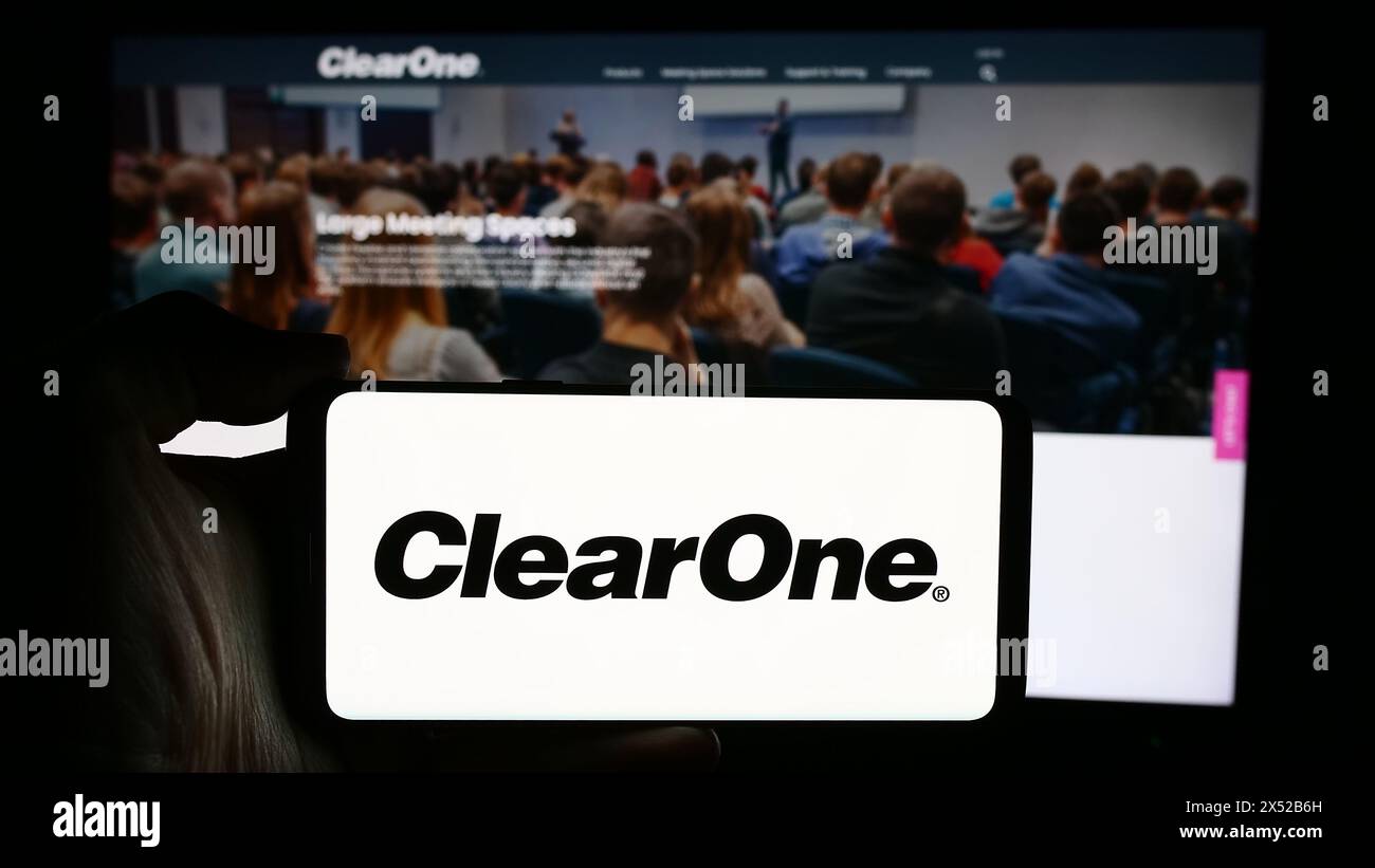 Person, die ein Mobiltelefon mit dem Logo des US-amerikanischen Konferenzlösungsunternehmens ClearOne Inc. Vor der Unternehmenswebseite hält. Schwerpunkt auf dem Display des Telefons. Stockfoto