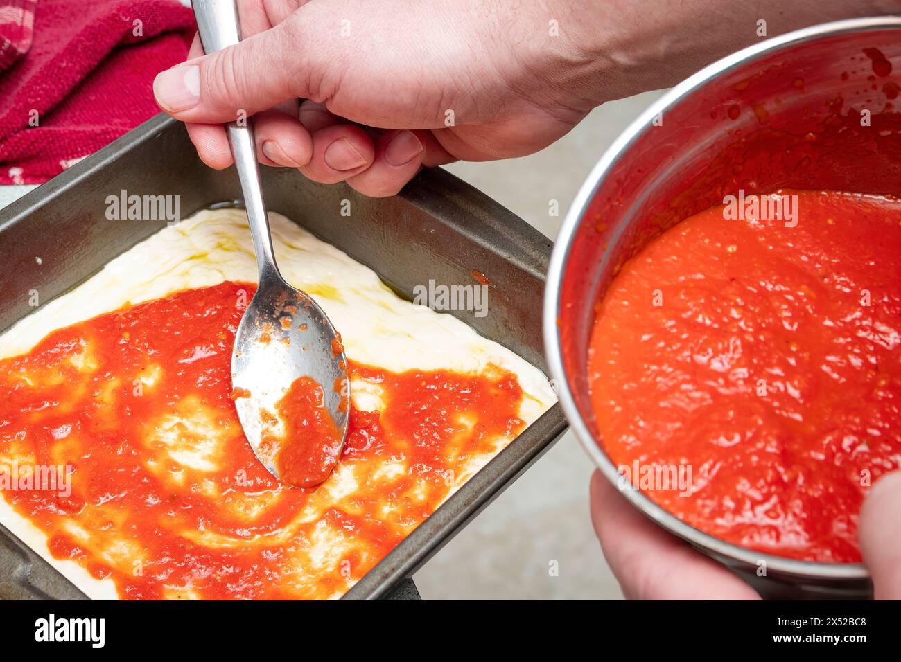 Frische Tomatensauce auf Pizzateig in der Pfanne löffeln, um Pizza nach Detroit-Art zuzubereiten. Stockfoto