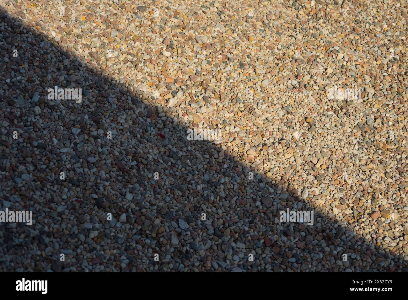 Eine Nahaufnahme von kleinen, bunten Kieselsteinen, die mit kontrastierenden diagonalen Schatten überlagert sind, wodurch ein dynamischer und strukturierter Hintergrund entsteht, der für künstlerische Zwecke geeignet ist Stockfoto