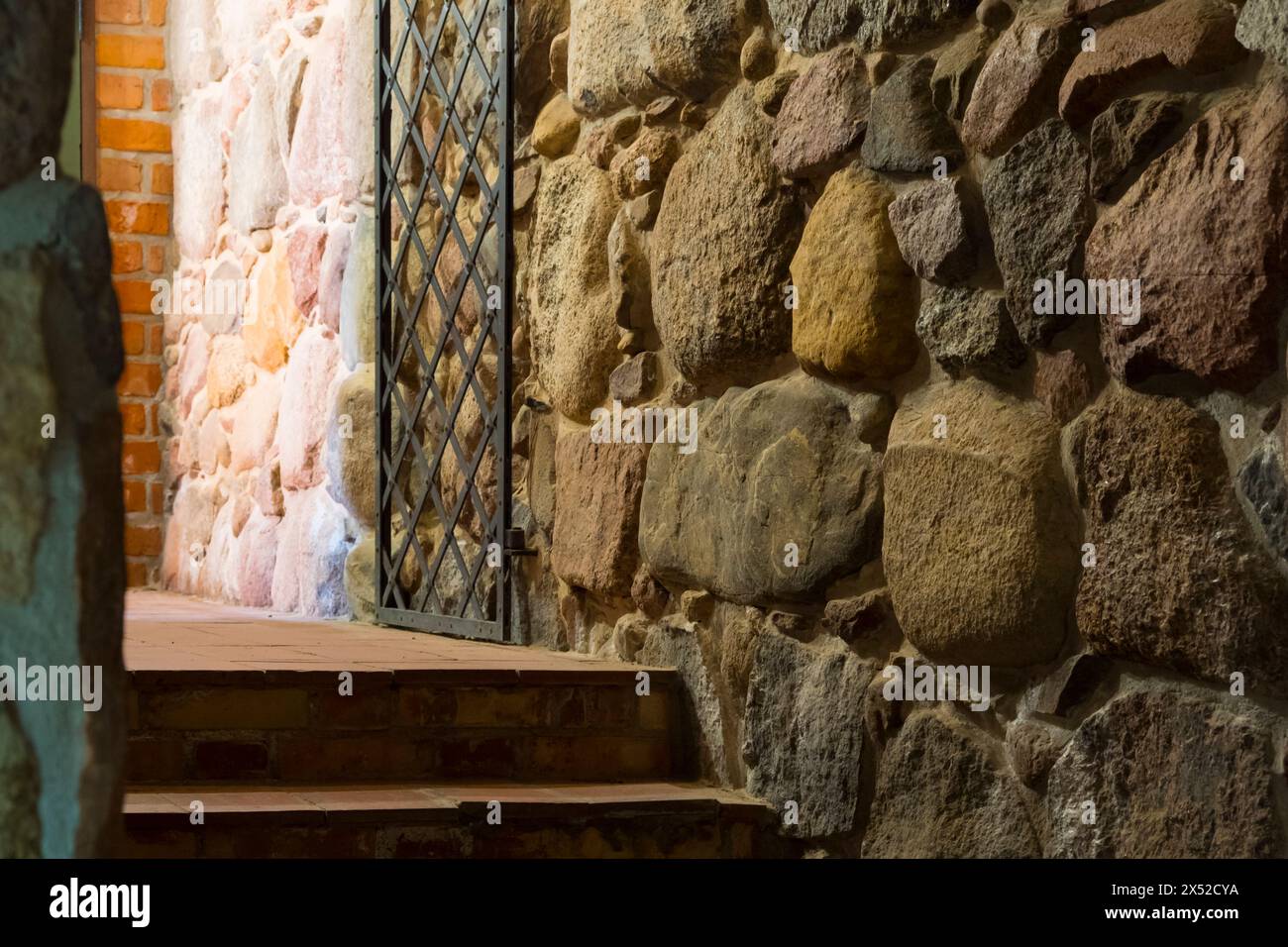 Eine alte Steinmauer mit einem vergitterten Fenster, die an die düstere Atmosphäre der Burgdungeons erinnert, perfekt für historische oder fantasievolle Hintergründe Stockfoto