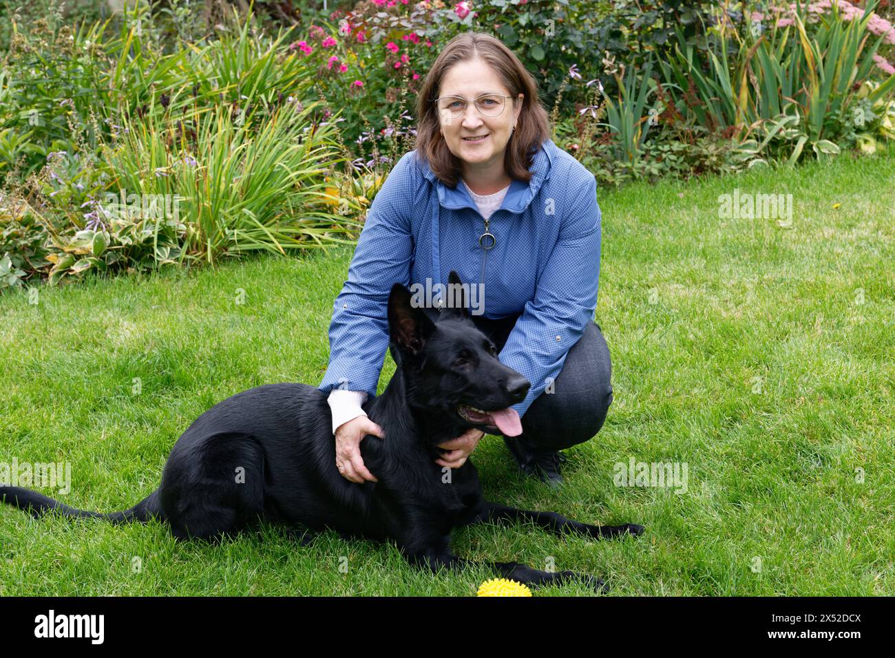 Eine Frau mit einem schwarzen Schäferhund auf einem grünen Rasen Stockfoto