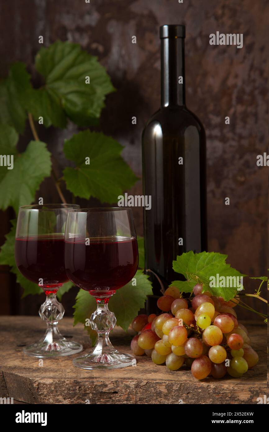 Das Konzept eines köstlichen alkoholischen Getränks, Wein und Trauben. Weinflasche, Gläser Rotwein und Trauben auf dunklem rustikalem Holzhintergrund mit Stockfoto