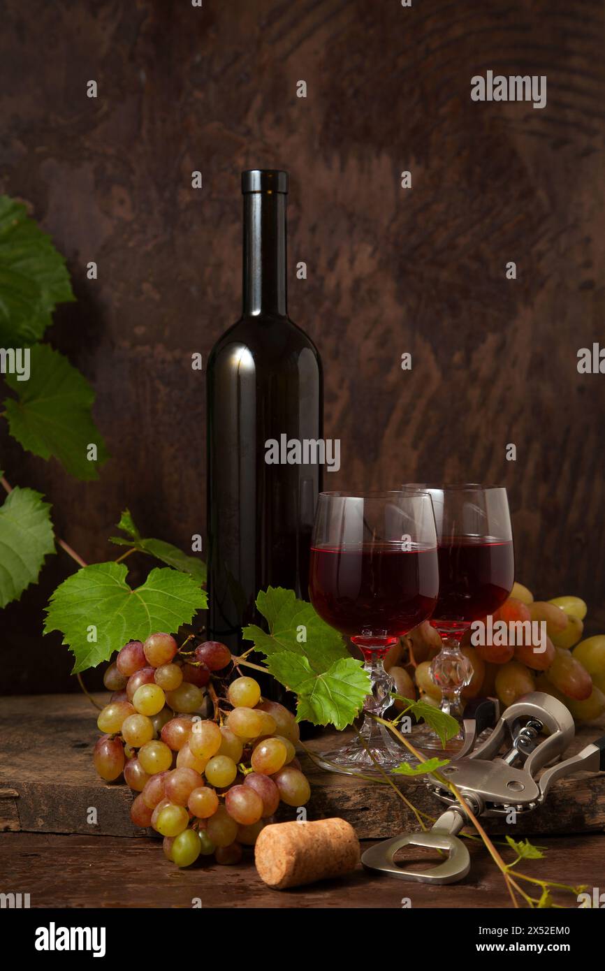 Das Konzept eines köstlichen alkoholischen Getränks, Wein und Trauben. Weinflasche, Kork, Korkenzieher, Gläser Rotwein und Trauben auf dunklem rustikalem wo Stockfoto