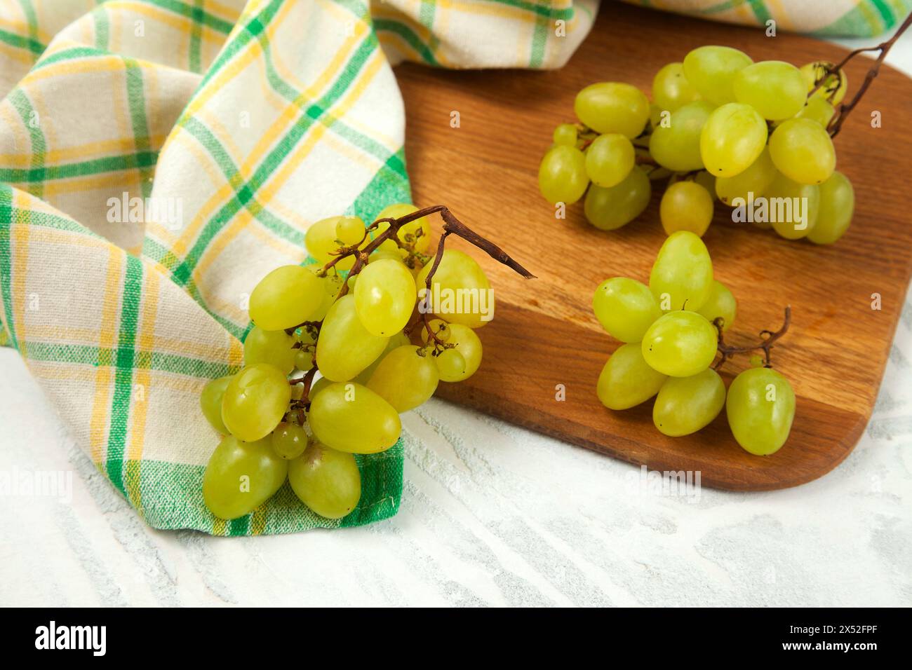 Schneidebrett mit einem großen Haufen reifer grüner Trauben auf weiß. Weißweintrauben mit grünem Küchentuch auf weißem hölzernem Hintergrund. Stockfoto