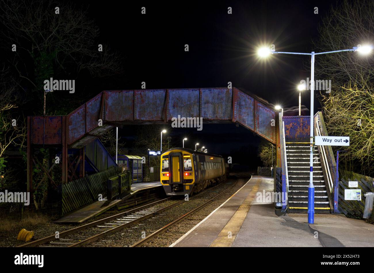 Ein Zug der Northern Rail-Klasse 158 158754 am Bahnhof Clapham, Yorkshire, auf der kleinen Nordwestlinie bei Nacht mit der Bahnhofsbrücke Stockfoto