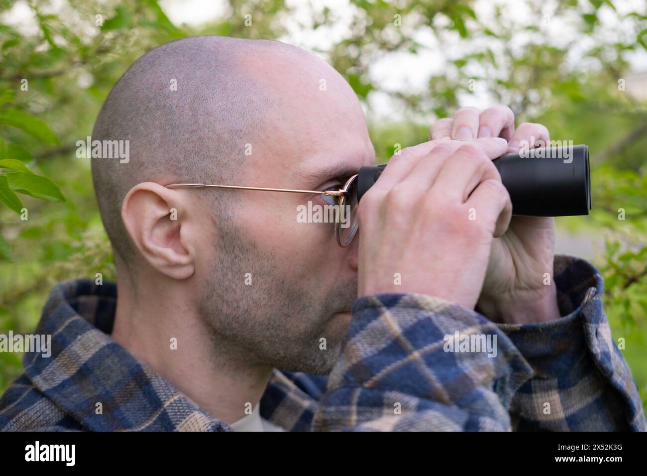 Junger Mann, versteckt in üppigem Grün, Spione bekleidet durch Ferngläser, Privatdetektiv überwacht, Nervenkitzel sucht das Ziel Stockfoto