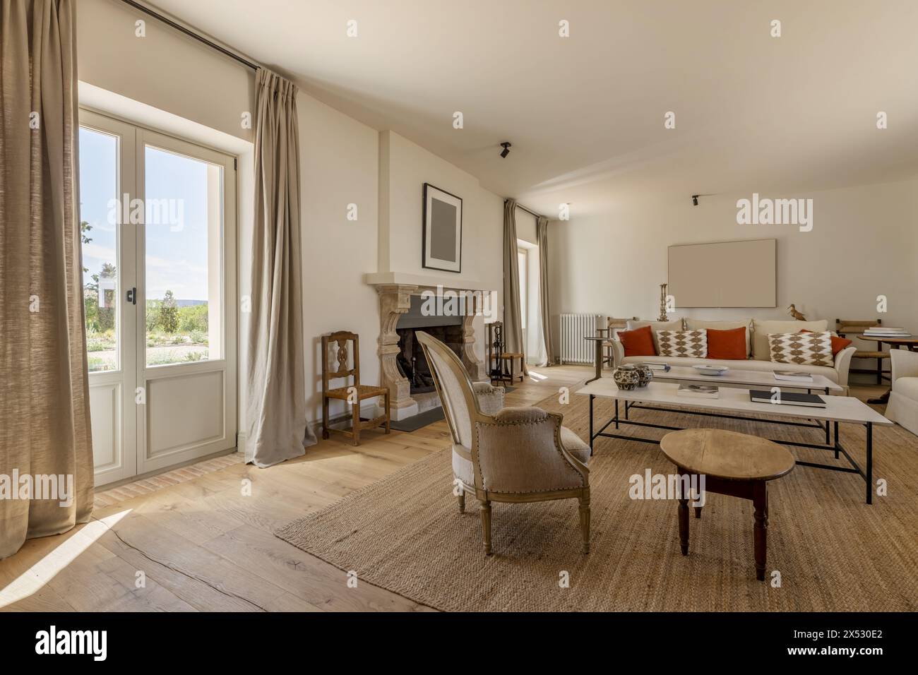 Ein großes Wohnzimmer mit Kamin mit Sesseln, Holzfußboden, Naturfaserteppich, weißen Kaffeetischen und wunderschöner moderner Dekoration wi Stockfoto