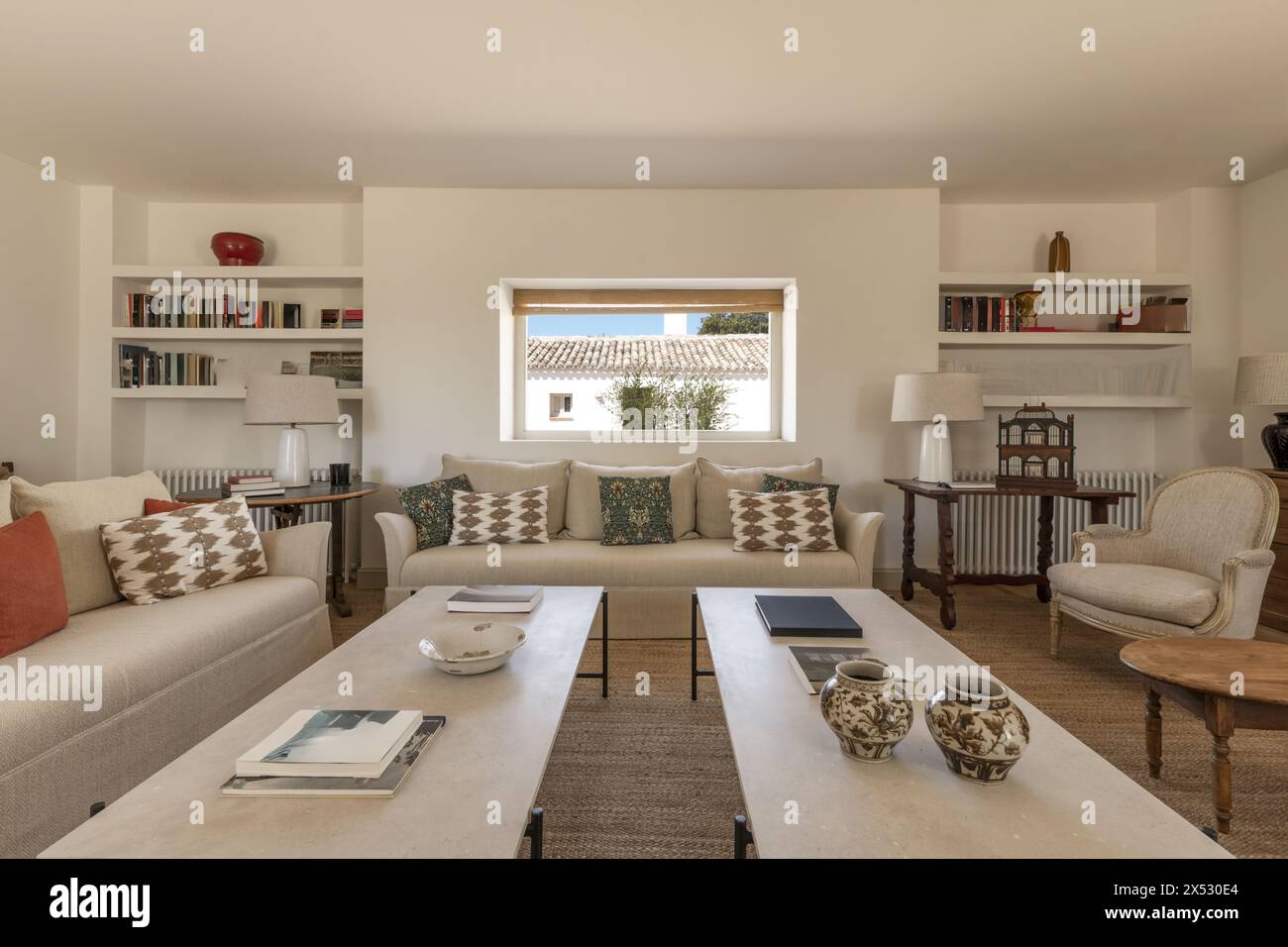 Ein großes Wohnzimmer mit einem Kamin mit großen beigefarbenen Stoffsofas, Holzböden, Naturfaserteppich, weißen Kaffeetischen und wunderschöner zeitgenössischer Atmosphäre Stockfoto