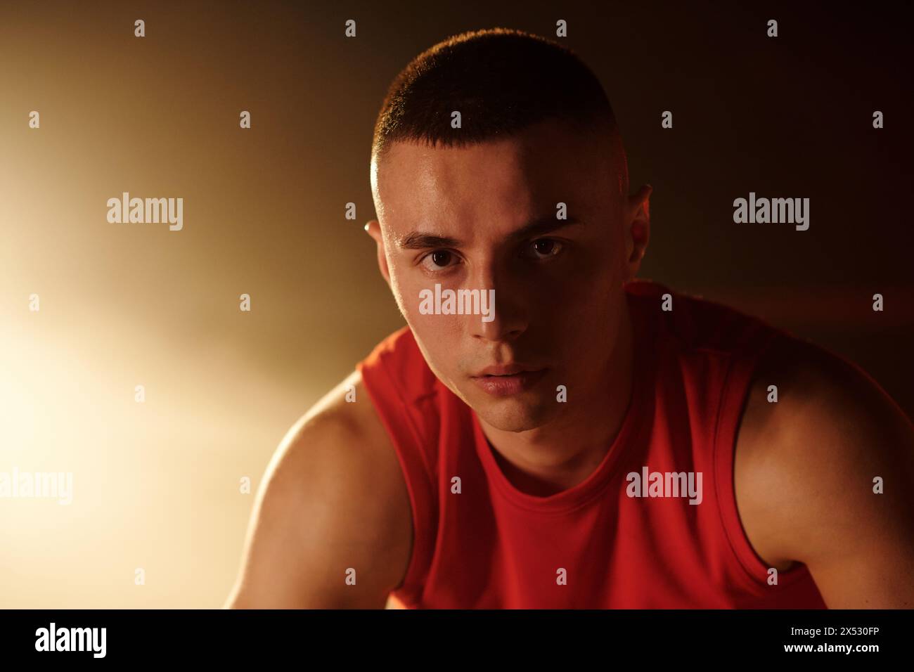 Junger Sportler in roter Sportbekleidung, der nach dem Training vor der Kamera auf dem Boxring steht und dich gegen Licht und Rauch ansieht Stockfoto