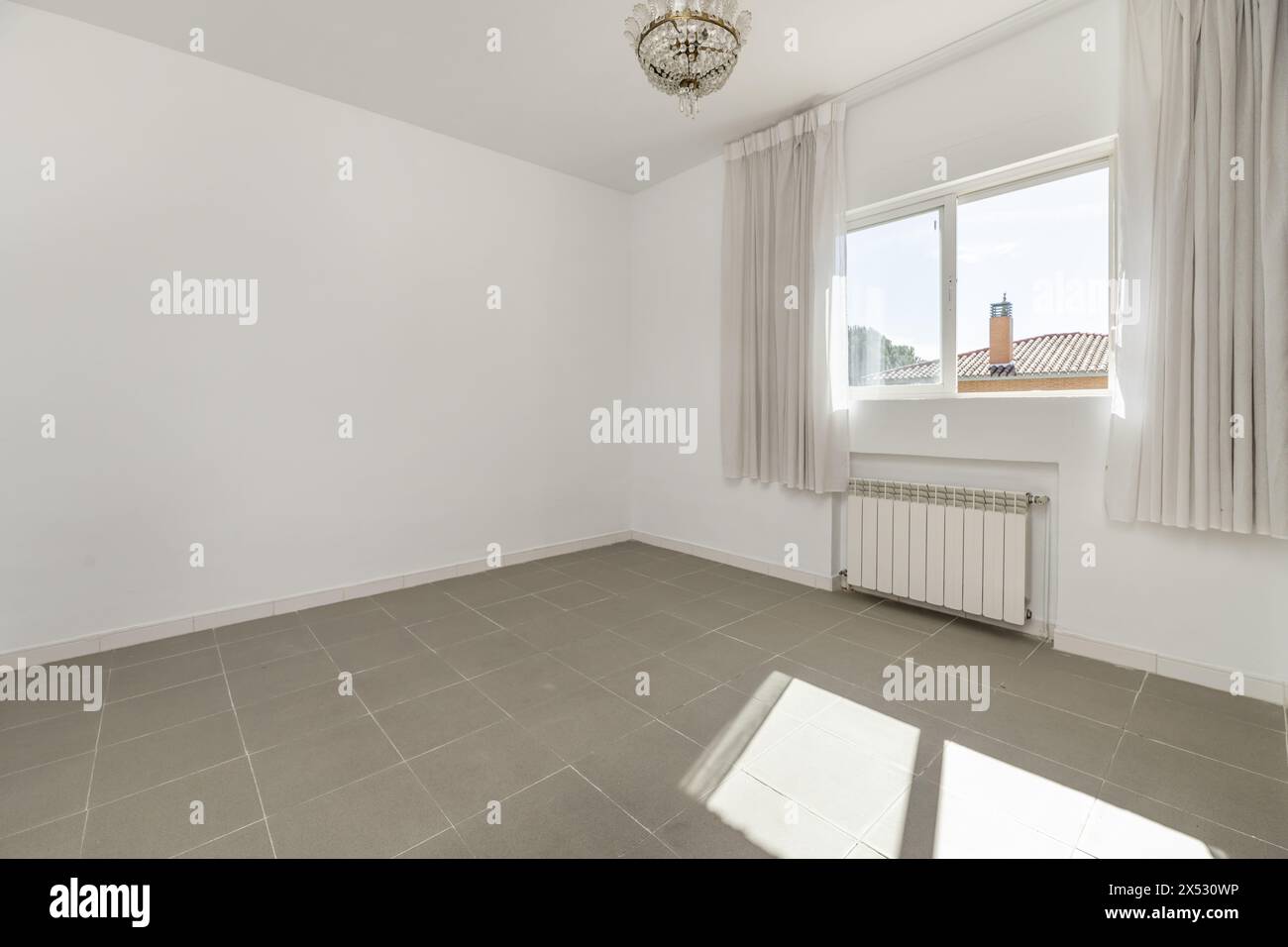 Ein großer leerer Raum mit glatten weißen Wänden und einem Fenster mit Vorhängen, durch das viel Licht hereinkommt Stockfoto