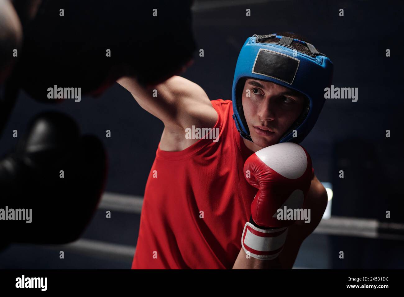 Junger Boxer im Schutzhelm, der seinen Rivalen ansieht und ihn beim Angriff oder bei der Verteidigung tretet, während er die Kampftechnik übt Stockfoto