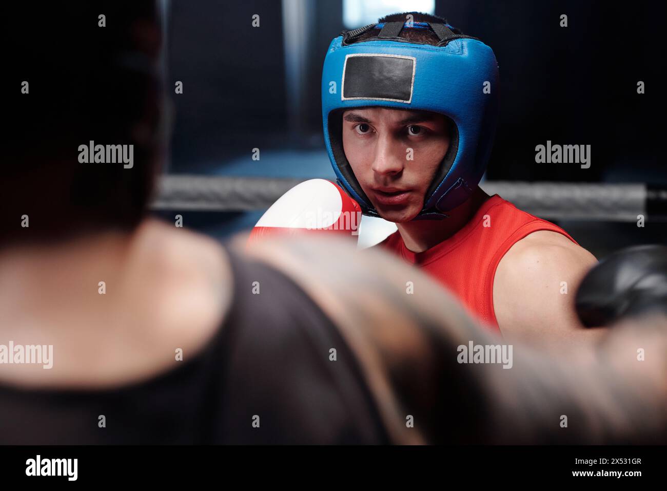 Junger ernsthafter Boxer im Schutzschild, der seinen Rivalen ansieht, der ihn angreift, und über den Schlag nachdenkt, während der Ringrunde Stockfoto