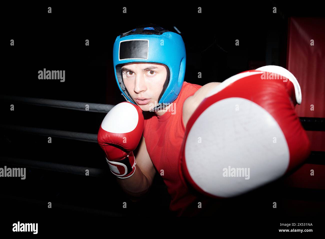 Junger Boxer schlägt seinen Rivalen mit der linken Hand in Boxhandschuhen und hält die Verteidigung durch die rechte während des Kampfes auf dem Boxring Stockfoto