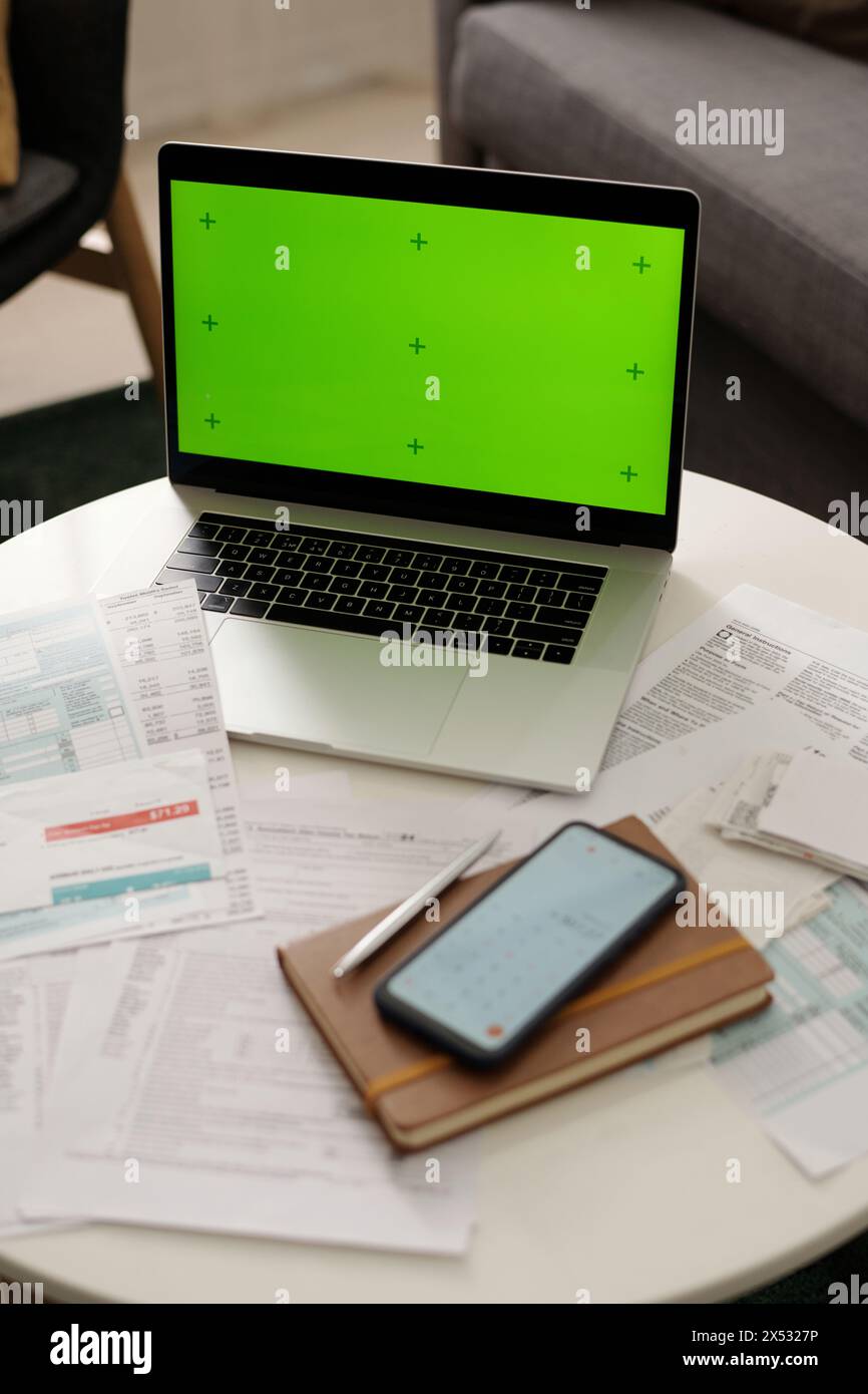 Hoher Winkel des Laptops mit Chroma-Taste auf dem Bildschirm, auf dem Tisch mit unbezahlten Rechnungen und Finanzpapieren, Notizblock und Smartphone Stockfoto