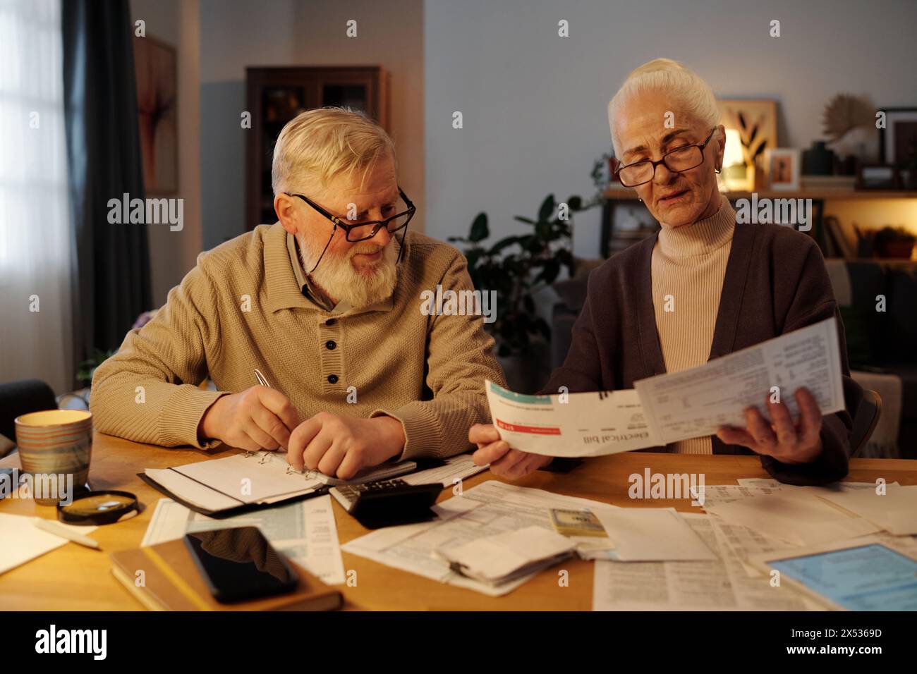 Seniorenpaar, das Zahlungsrechnungen in den Händen einer älteren Frau betrachtet, während er Finanzdaten in der häuslichen Umgebung überprüft und bespricht Stockfoto