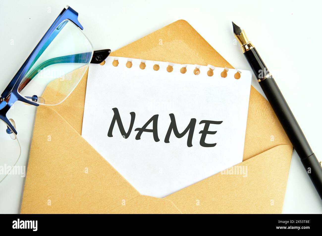 Ein Wort namens eine Inschrift auf einem Stück Papier, das aus einem Umschlag neben Gläsern und Bleistiften blickt Stockfoto