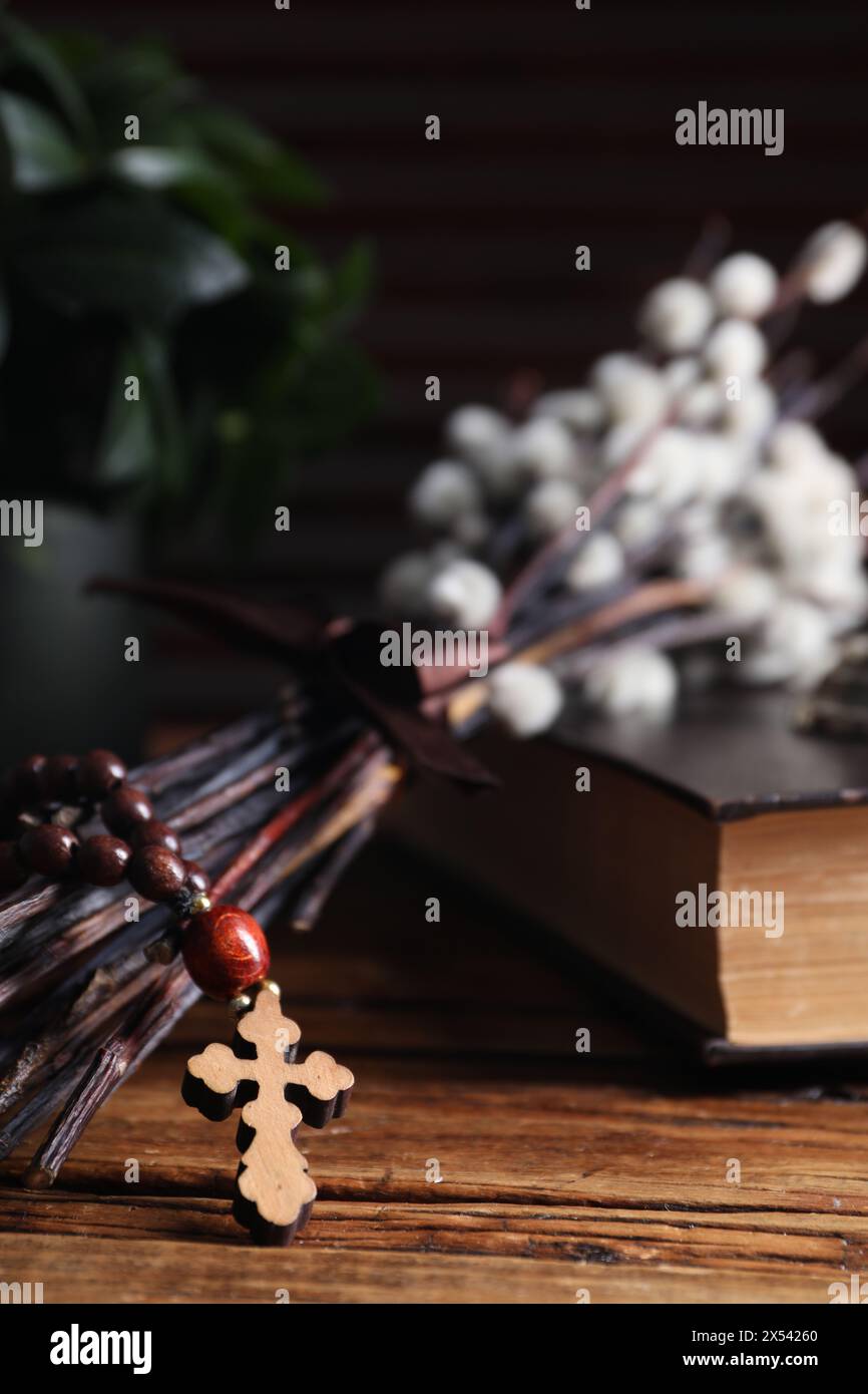 Rosenkranzperlen, Bibel und Weidenzweige auf Holztisch, Nahaufnahme Stockfoto