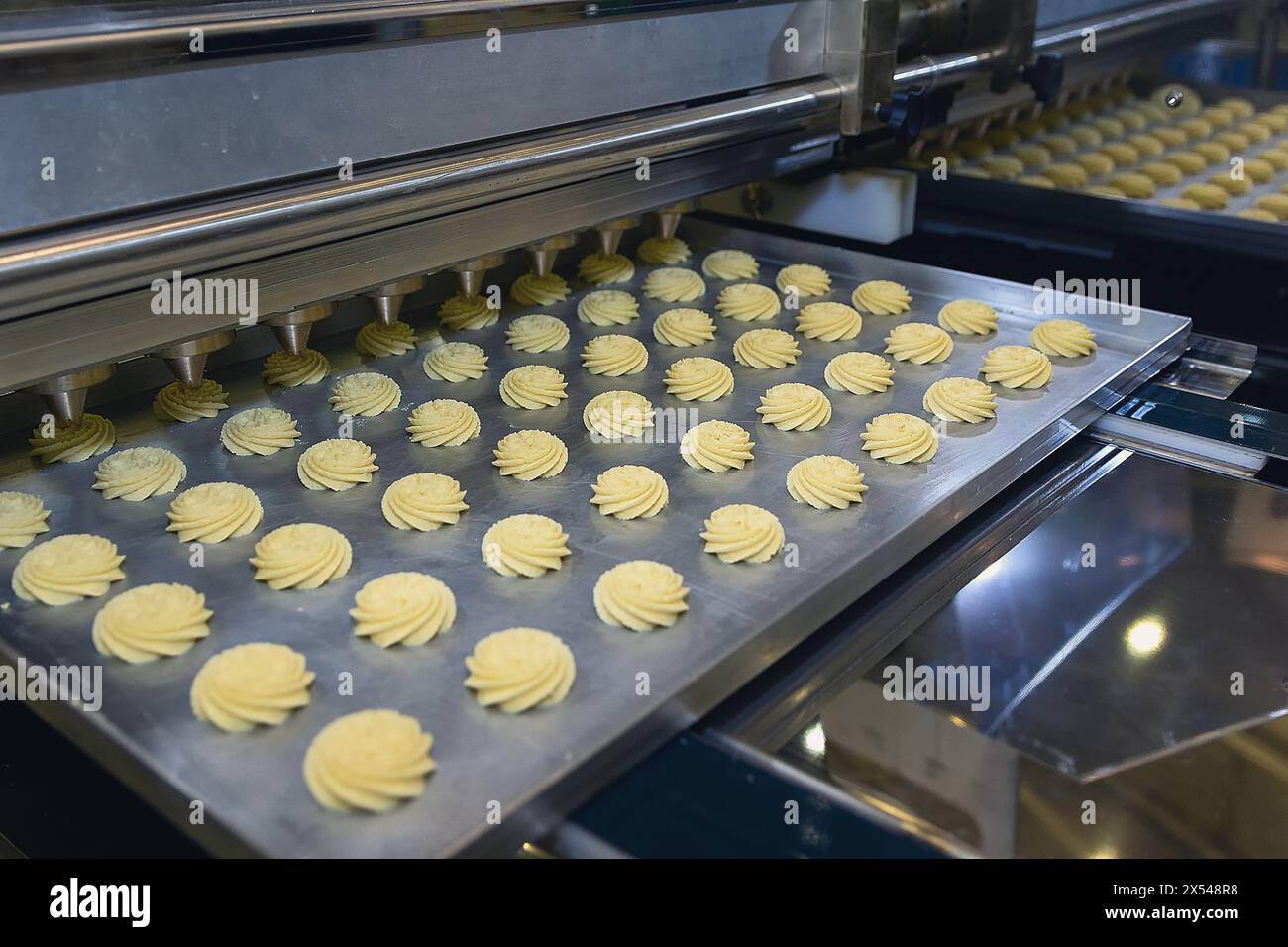 Eine Fördermaschine gießt Sahne auf Kekse. Fabrik für die Herstellung von Keksen und gebackenen Keksen Stockfoto