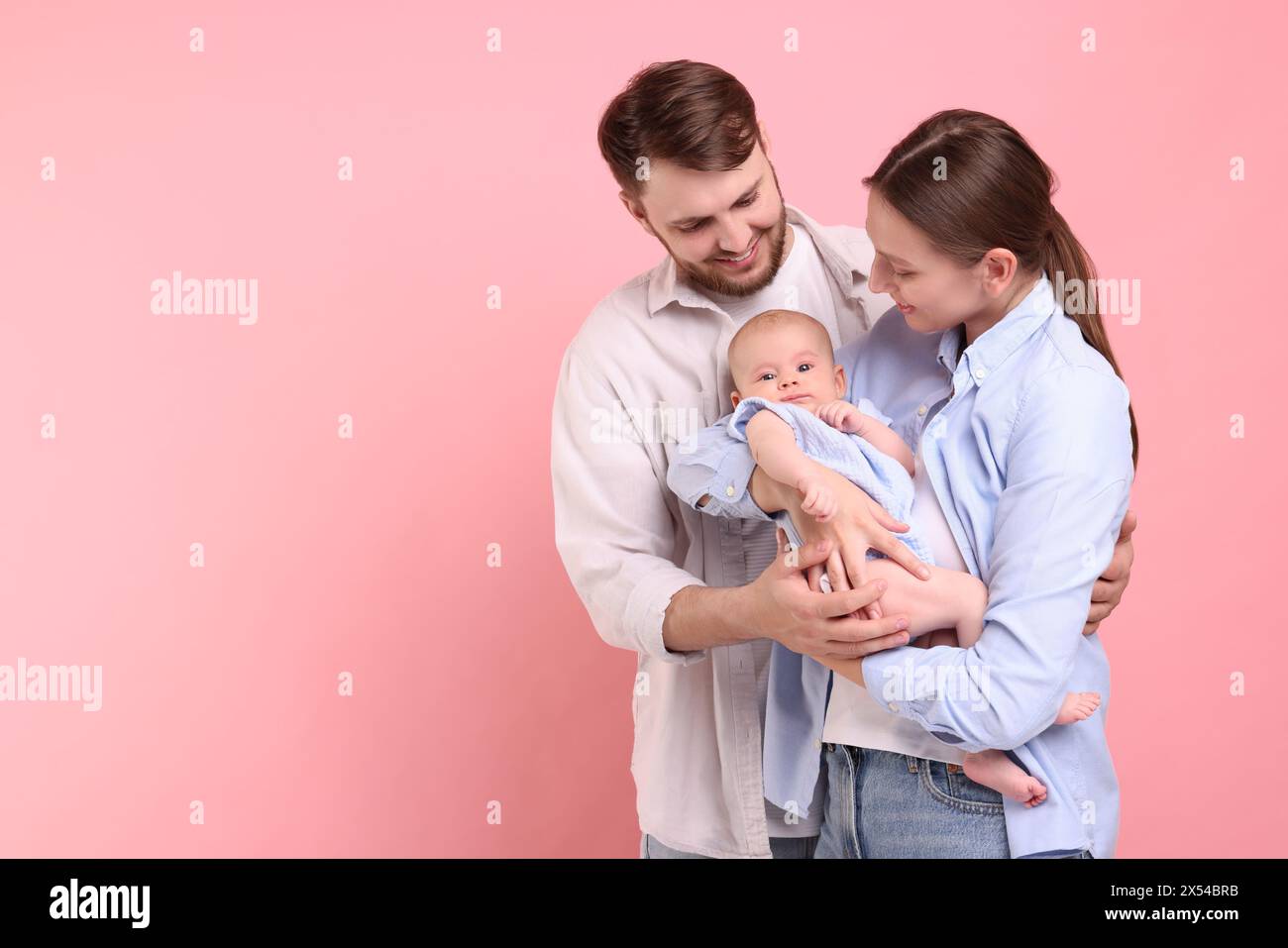 Glückliche Familie. Eltern mit ihrem süßen Baby auf rosa Hintergrund, Platz für Text Stockfoto