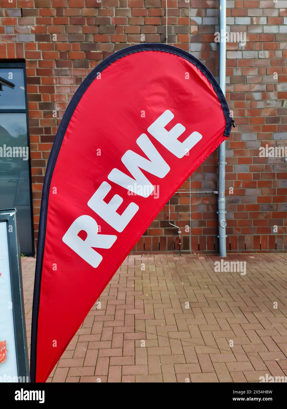 Kiel, Deutschland - 04. Mai 2024: Eine Flagge mit dem Logo der Rabattkette REWE vor dem Eingang einer Supermarktfiliale Stockfoto