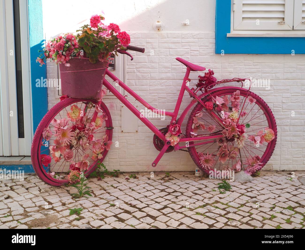 Rosafarbenes Damenfahrrad mit Blumen in Rädern und Korb, um die Unterkunft in Olhão, Portugal, hervorzuheben. Stockfoto