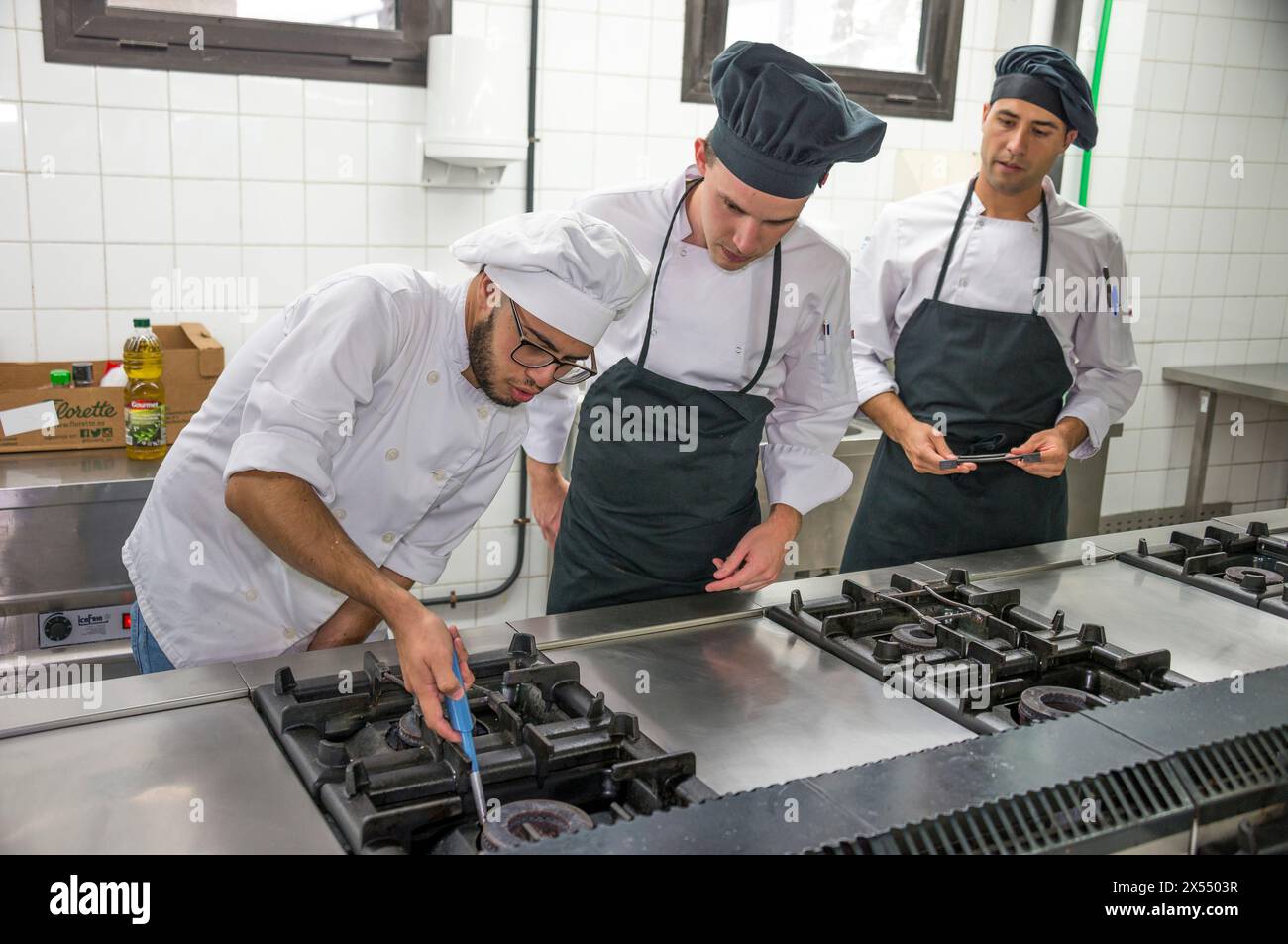 Koch und Assistenten, die eine Industrieküche beleuchten Stockfoto
