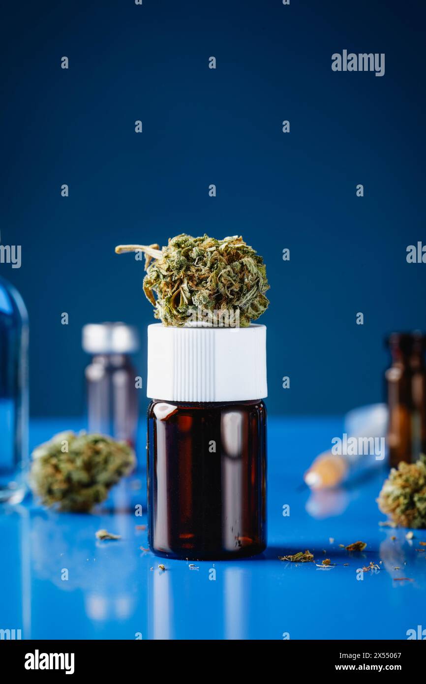 Eine Cannabisknospe auf einer Flasche, auf einem blauen Tisch, neben einigen anderen Cannabisknospen und -Flaschen Stockfoto