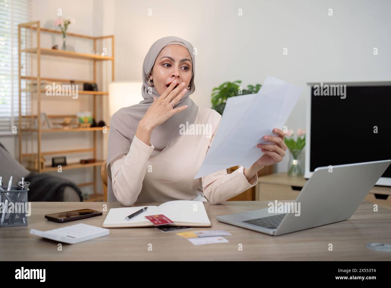 Junge beunruhigte und schockierte muslimische Frau im Hijab mit Dokumenten und Taschenrechner. Finanzielle Probleme mit Konten, Krediten, Familienhaushalt zu Hause Stockfoto