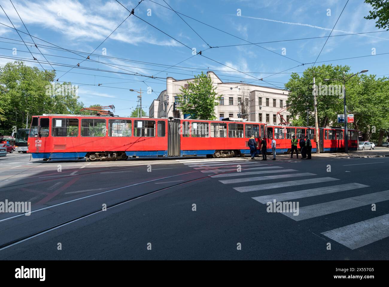 Die traditionelle rote elektrische Belgrader Straßenbahn entgleiste und hielt den Verkehr auf, die Mitarbeiter arbeiten daran, sie wieder auf Kurs zu bringen. Mai 2024 Stockfoto