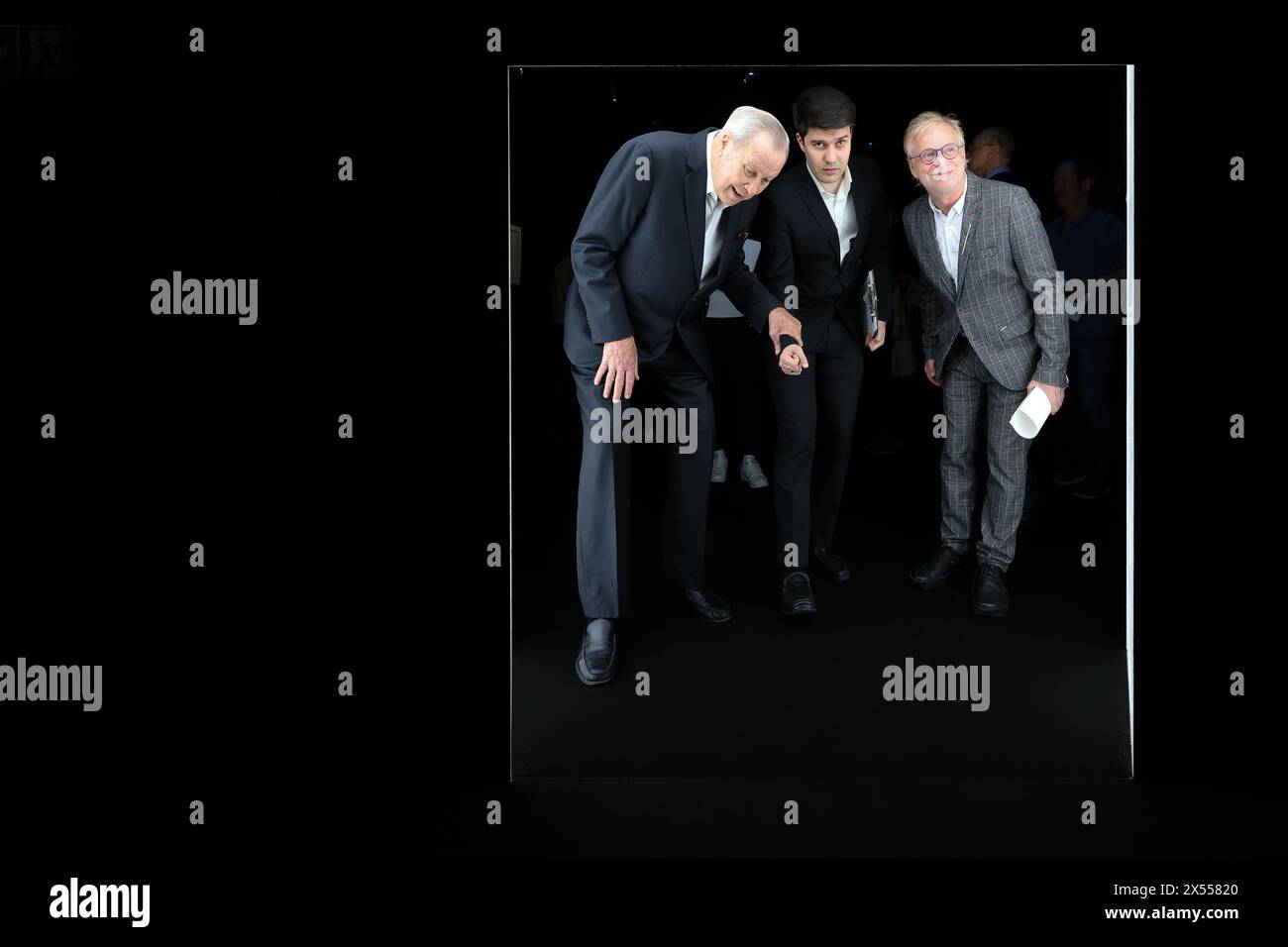 07. Mai 2024, Sachsen, Leipzig: Robert Wilson (l-r), US-amerikanischer Regisseur und Künstler, seine Assistentin Liam Krumstroh und Olaf Thormann, Direktor des GRASSI Museums für Angewandte Kunst, gehen durch eine sehr niedrige Eröffnung in der Ausstellung „A Chair and You“ im Grassi Museum für Angewandte Kunst. Die Show wirft einen Blick auf eine der weltweit wichtigsten privaten Stuhlsammlungen. Die rund 140 Stühle, deren skulpturaler Charakter weit über die übliche Typologie der Stühle hinausgeht, wurden vom Genfer Unternehmer und Sammler Barbier-Mueller zusammengeführt. Bis zum 6. Oktober können die Besucher die Werke von More besichtigen Stockfoto