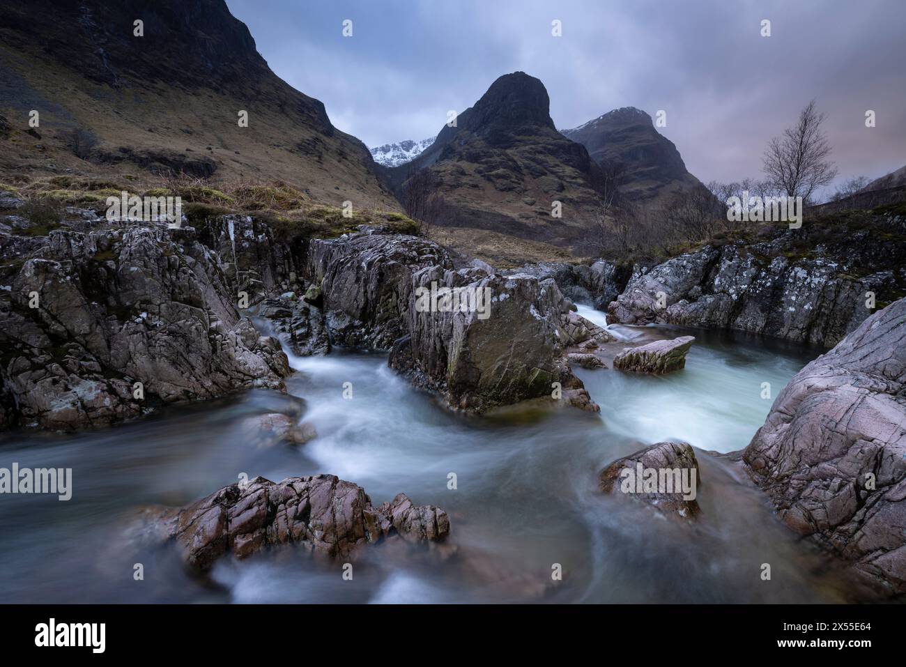 Der Fluss Coe rauscht durch eine Schlucht unterhalb der Three Sisters of Glencoe Mountains in Glencoe, Schottland, Großbritannien. Frühjahr (März) 2024. Stockfoto